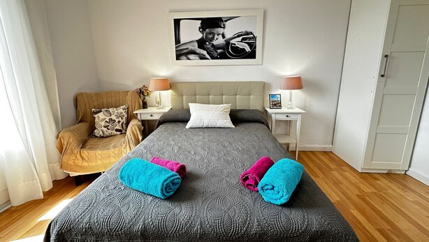 Una habitación de hotel con una cama, dos mesitas de noche, una silla y un armario.