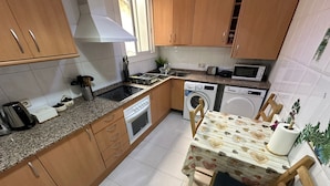 Une cuisine compacte avec des meubles en bois, un four encastré, un four à micro-ondes et un lave-linge.