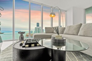 Un salon moderne avec une table basse en verre, un canapé et une vue sur les gratte-ciel de la ville, visible à travers de grandes fenêtres.