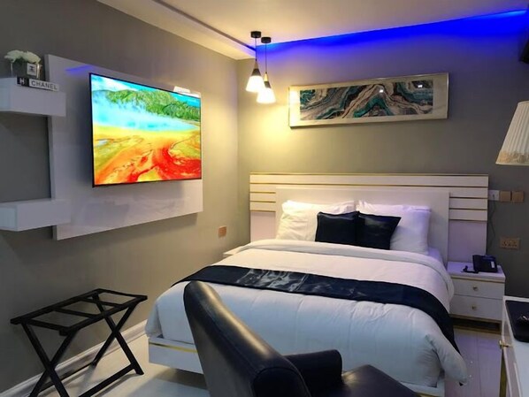 A modern bedroom with a large bed, a flat-screen TV mounted on the wall, a bedside table, and a small desk. - Republican City Apartment (Awka)