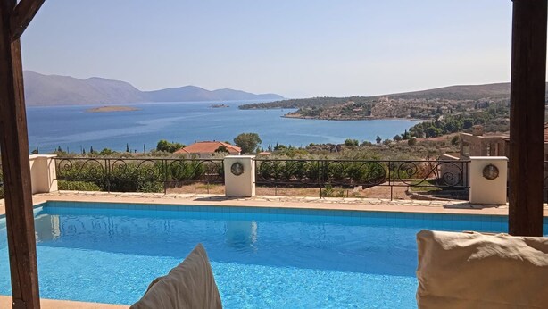 A pool with a view of a coastal landscape, including mountains and a body of water.