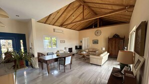 A spacious living area with a high wooden ceiling, a dining table, a sofa, and a TV.