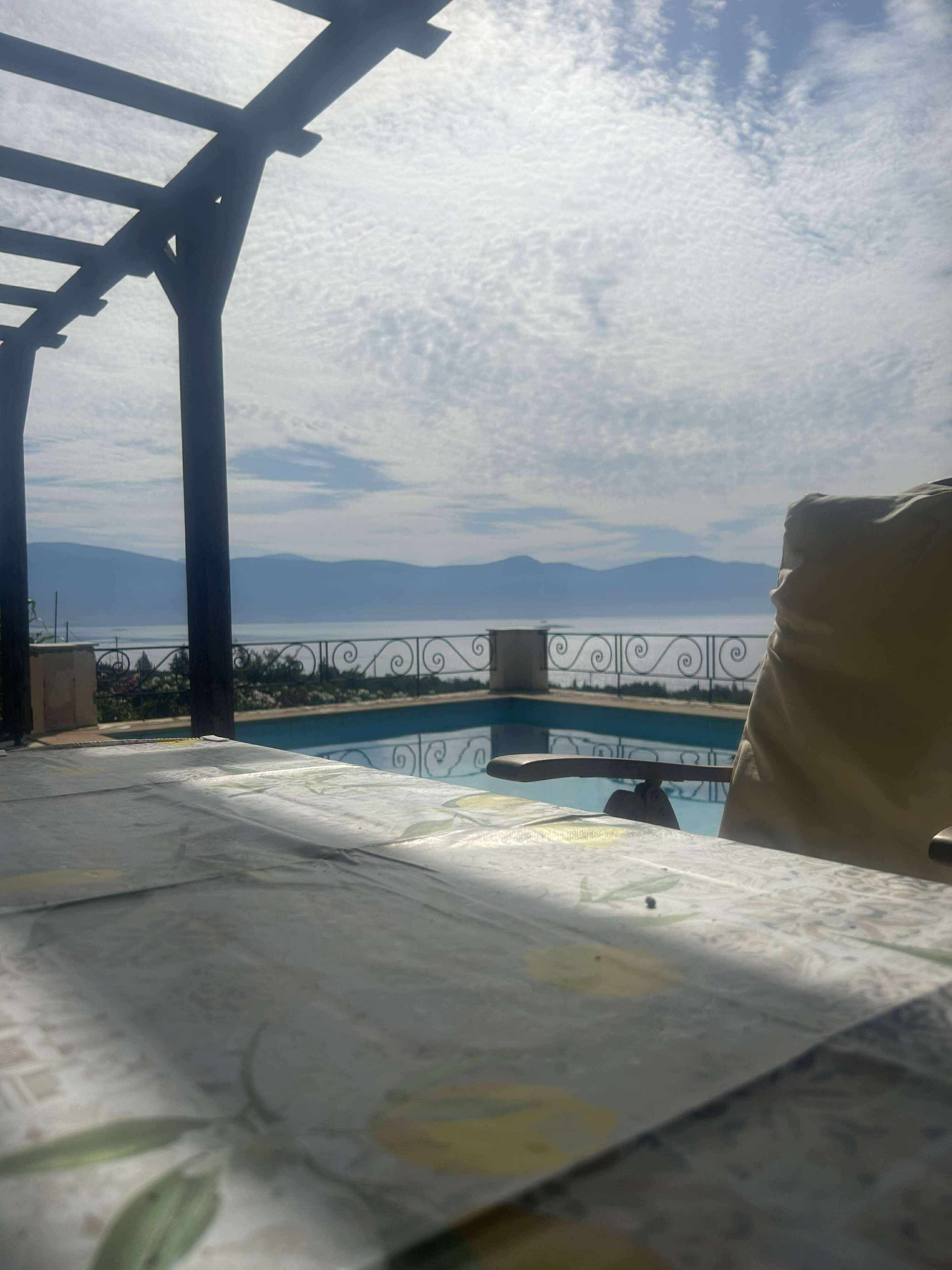A pool area with a pergola structure, a view of mountains, and a clear sky.