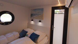 Un dormitorio con cama, una ventana redonda, un cuadro y un equipo de aire acondicionado.