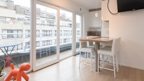 A modern kitchen with a large window, a dining area with a table and chairs, and a small orange toy on the floor. - Apartment in Ostend Near Beach (Ostend)