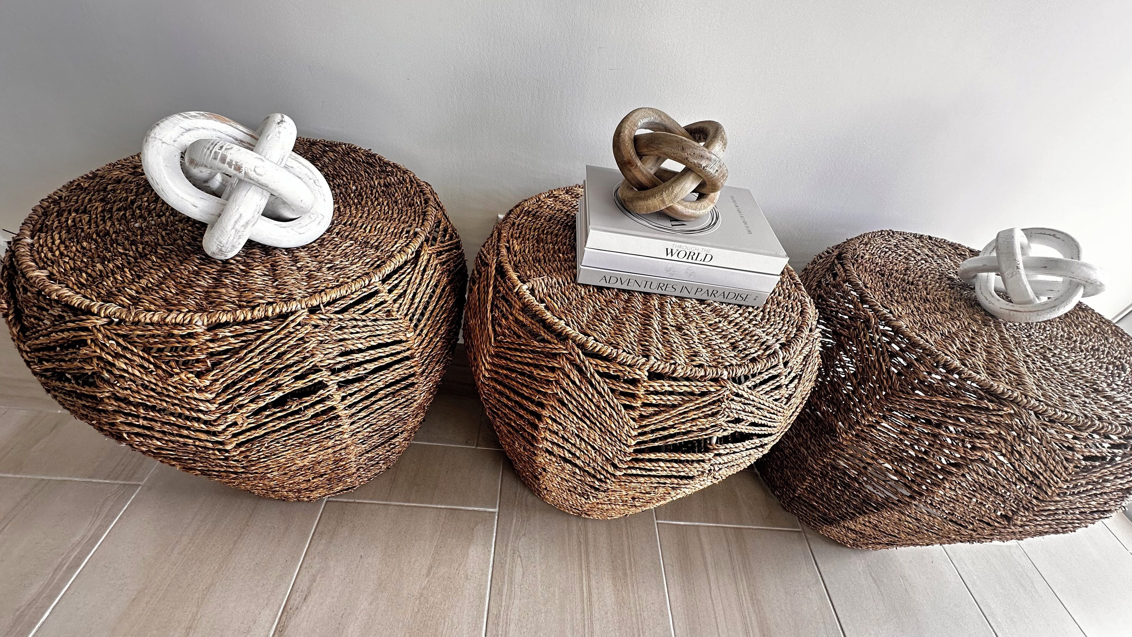 Drie ronde geweven poefs met verschillende decoratieve bovenkanten, geplaatst op een betegelde vloer tegen een effen muur.