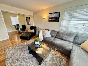 A modern living room with a grey sofa, a glass coffee table, and a black leather chair. - Top-Rated Bungalow Near City Park/National Jewish (Denver)