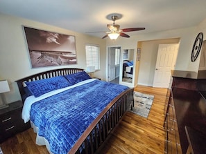 A bedroom with a bed, a ceiling fan, a wooden floor, a door, and a wall-mounted clock. - Top-Rated Bungalow Near City Park/National Jewish (Denver)
