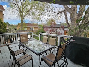 Une terrasse dotée d’une table avec un plateau en verre, de quatre chaises et d’un barbecue.