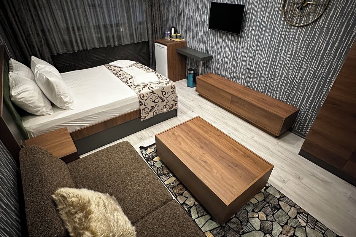 A modern bedroom with a bed, sofa, and coffee table, featuring a stone-patterned rug and a flat-screen TV mounted on the wall.