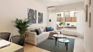 A modern living room with a sofa, two side tables, a potted plant, and a view of an outdoor seating area through a glass door. - Laia Deluxe Terrace Apartment (Barcelona)