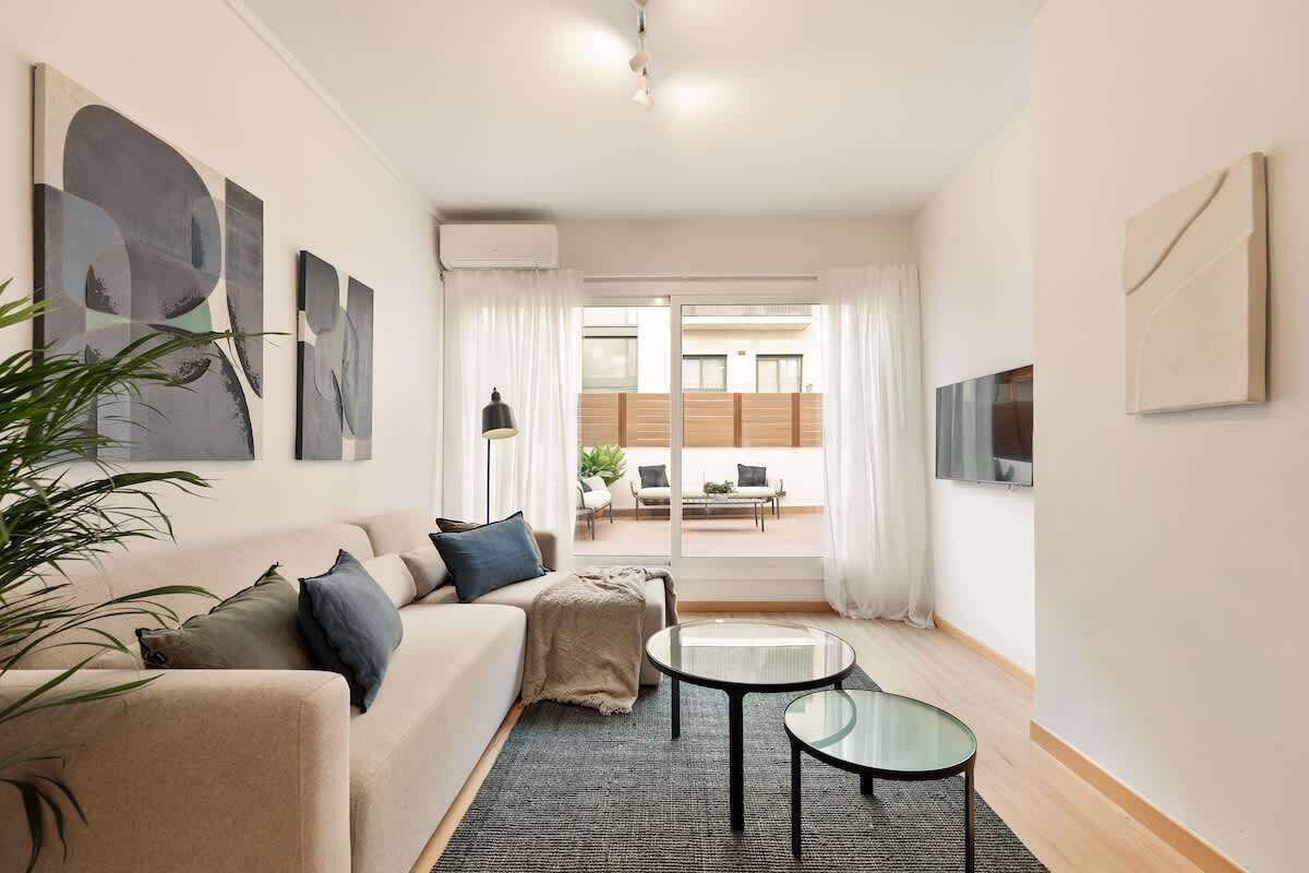 A modern living room with a beige sofa, a glass coffee table, and abstract wall art.