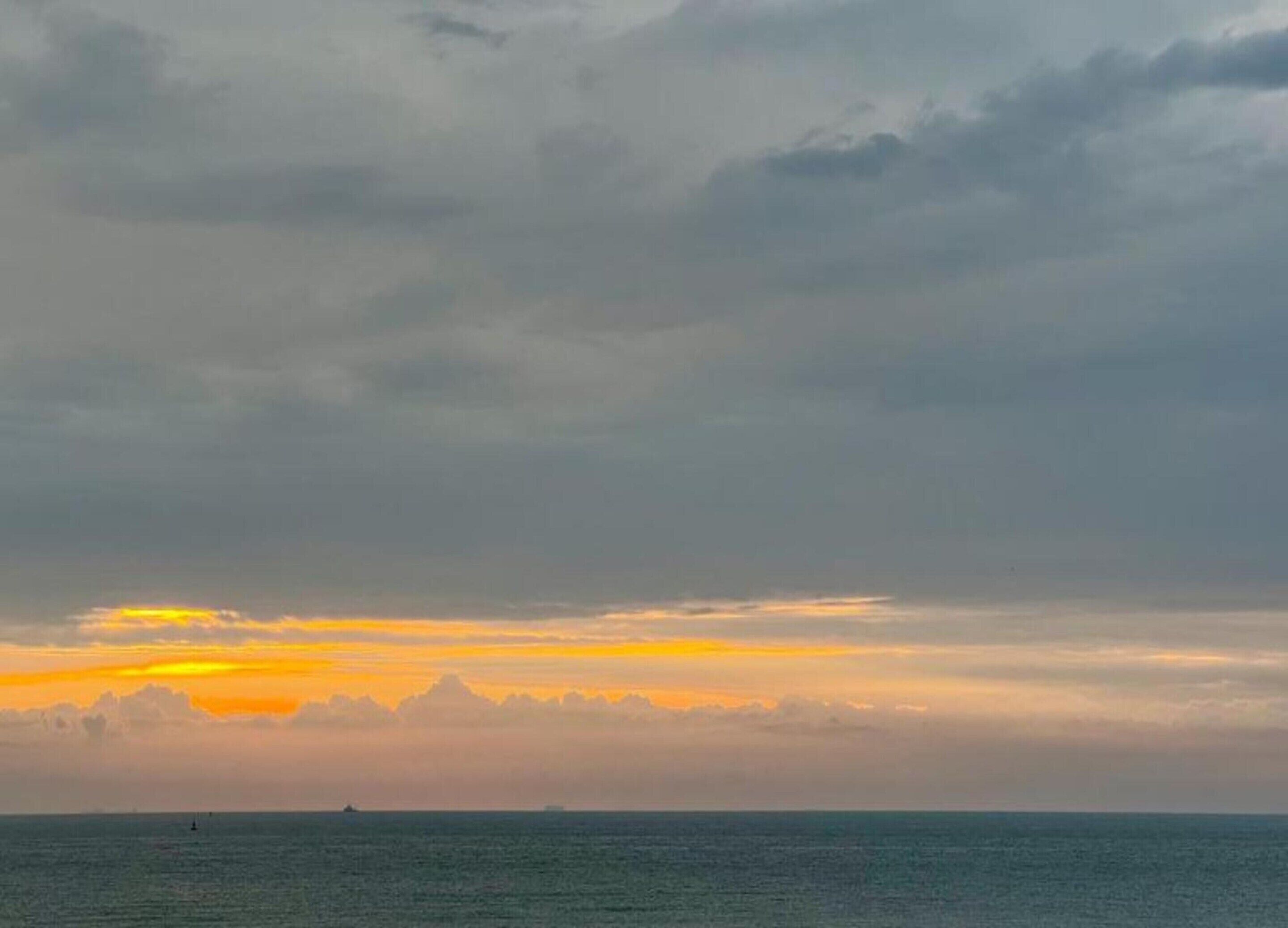 A sunset over the ocean with a distant ship and a small buoy.