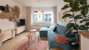 A modern living room with a sofa, a TV, a coffee table, and a large plant. - Apartment in Ostend Near the Beach (Ostend)
