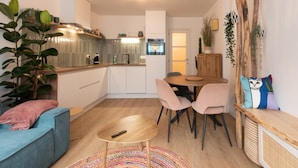 A modern living room with a blue sofa, a wooden coffee table, and a dining area with a wooden table and chairs. - Apartment in Ostend Near the Beach (Ostend)