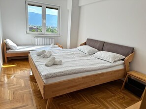 A bedroom with a wooden bed, a window with a view, and a small bedside table. - Air Urban 4-room apartment, balcony, parking, air-conditioned and fully equipped (Sarajevo)