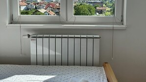 A bedroom with a large window overlooking a cityscape and mountains. - Air Urban 4-room apartment, balcony, parking, air-conditioned and fully equipped (Sarajevo)