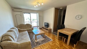 A modern living room with a sofa, a coffee table, a TV, and a dining area with chairs. - Air Urban 4-room apartment, balcony, parking, air-conditioned and fully equipped (Sarajevo)