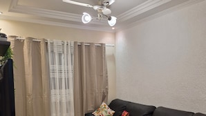 A living room with a black sofa, a ceiling fan, a TV, and a remote control on a stand. - Apartment in KAZAPAZ GUILHERMINA, 73m². Plenty of shops nearby. (Guilhermina Praia Grande)