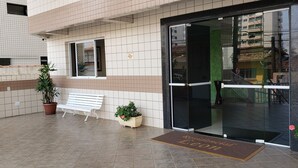 A building entrance with a bench, potted plants, and a doormat. - Apartment in KAZAPAZ GUILHERMINA, 73m². Plenty of shops nearby. (Guilhermina Praia Grande)