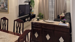 A living room with a TV, a dining table, chairs, a sofa, a ceiling fan, and a painting on the wall. - Apartment in KAZAPAZ GUILHERMINA, 73m². Plenty of shops nearby. (Guilhermina Praia Grande)