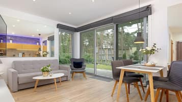 A modern living room with a sofa, a dining table with chairs, and a large window offering a view of the outdoors.
