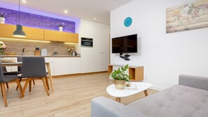 Ein modernes Wohnzimmer mit grauem Sofa, einem Essbereich mit Tisch und Stühlen, einer Küche mit weißen Schränken, einem flachbildfernseher an der Wand und einer Weltkarte.
