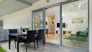 Eine moderne Terrasse mit Esstisch und Stühlen, eine Glastür, die zu einem Innenraum führt, und eine kleine Sitzgelegenheit im Freien.