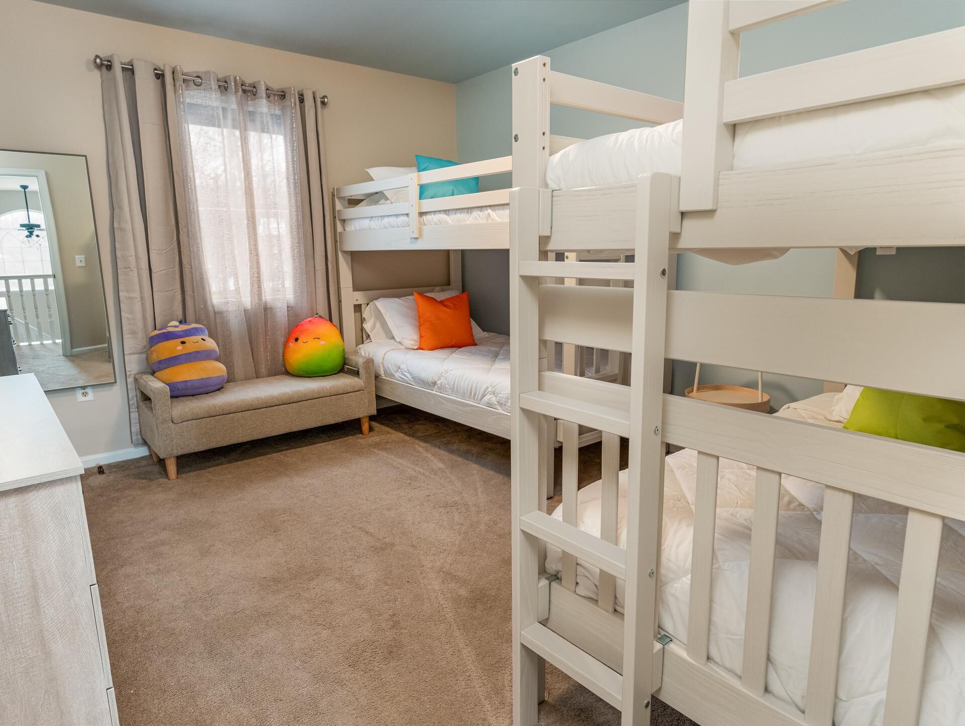 Une chambre d’enfant avec des lits superposés, un canapé et un pouf coloré.