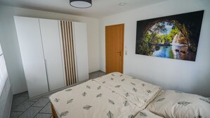 A bedroom with a bed, a wardrobe, a door, and a wall-mounted painting. - Vacation apartment with cozy terrace in the northern Black Forest (Oberreichenbach)