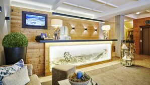 Un espace d’accueil doté d’un comptoir de réception en bois, d’un téléviseur fixé au mur et d’un grand tableau représentant un paysage de montagne.