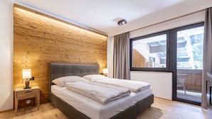 Une chambre moderne avec un mur en bois, un grand lit, une table de chevet et une fenêtre donnant sur l’extérieur.