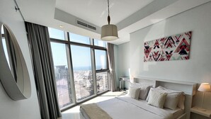 A modern bedroom with a large bed, a view of the city, and a geometric wall art piece. - Lux BnB Paramount Ocean View (Dubai)