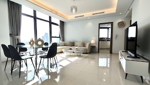 A modern living room with a dining area, large windows, and a television. - Lux BnB Paramount Ocean View (Dubai)