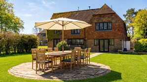 A brick house with a stone patio, a wooden table with chairs, and a large umbrella. - Spacious East Sussex retreat with tennis court, hot tub, and room for 24 (Whitesmith)