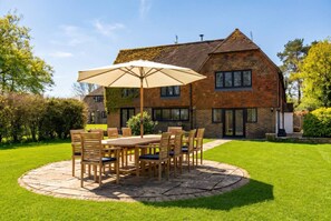 A brick house with a stone patio, a wooden table with chairs, and a large umbrella. - Spacious East Sussex retreat with tennis court, hot tub, and room for 20 (Whitesmith)