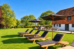 Een zwembadgedeelte met ligbedden en parasols, een terras met tafels, en een gebouw met een betegeld dak.