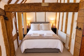 Een slaapkamer met een houten plafond, een bed met wit beddengoed, twee bedlampen en een bordje boven het bed.