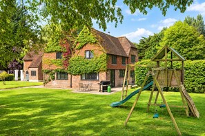 Een bakstenen huis met een groene glijbaan en een schommel in de voortuin.