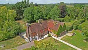 A large, traditional house with a brick exterior and multiple chimneys, surrounded by lush greenery and trees. - Spacious East Sussex retreat with tennis court, hot tub, and room for 24 (Whitesmith)