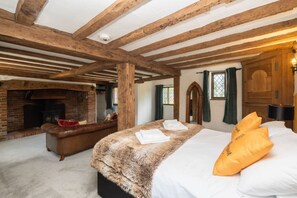 A room with exposed wooden beams, a fireplace, a bed with a fur throw, and a bench.