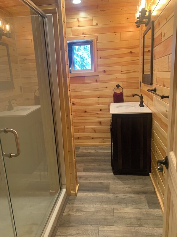 A wooden cabin bathroom with a glass shower enclosure, a window, and a sink with a mirror.