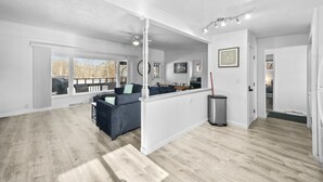 Amplia sala de estar con un sofá de color oscuro, una mesa de comedor y una zona de cocina con un cubo de basura de acero inoxidable.
