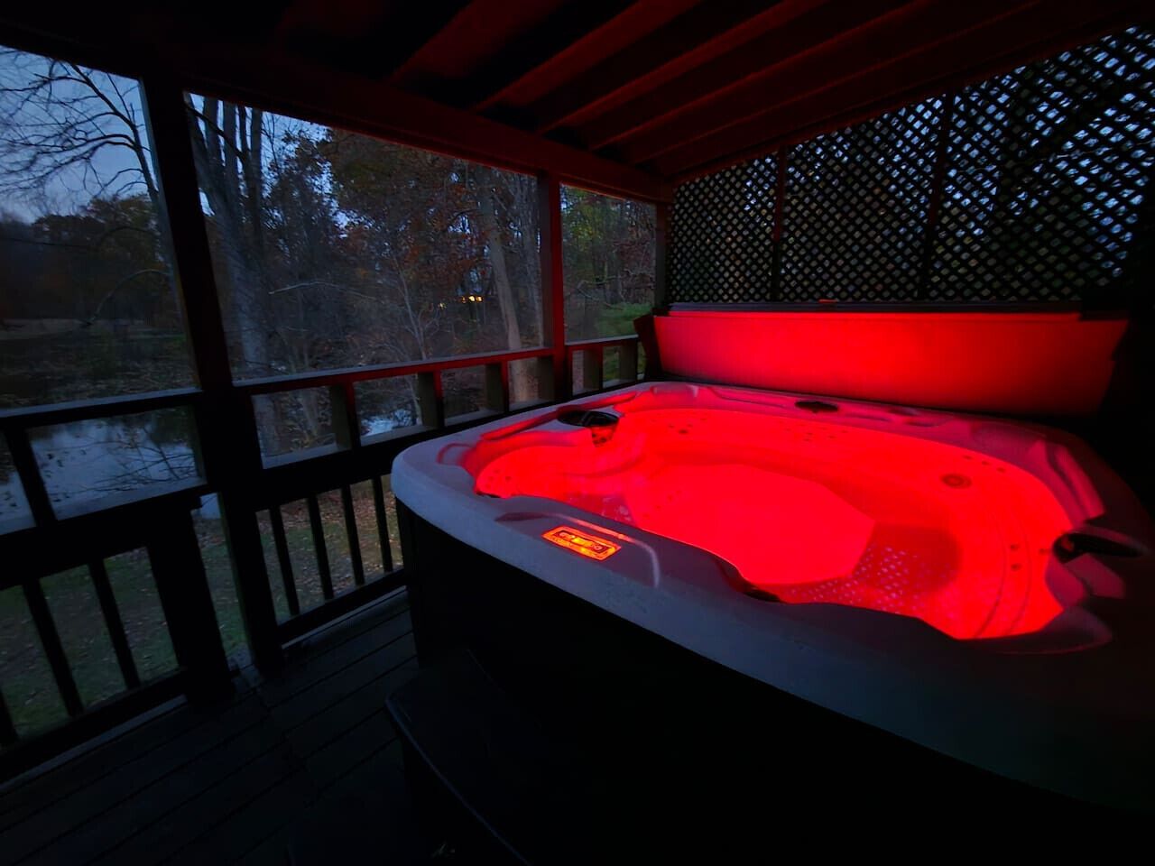 Un bain à remous éclairé d’une lumière rouge, entouré d’une terrasse en bois et d’une clôture à treillis.