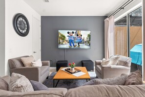 Una sala de estar moderna con un televisor de pantalla plana, dos sofás, una mesa de centro y un ventanal grande.