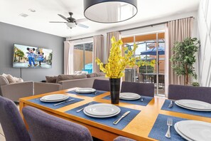 Un comedor con una mesa dispuesta para cuatro personas, un televisor montado en la pared y un balcón con mobiliario exterior.
