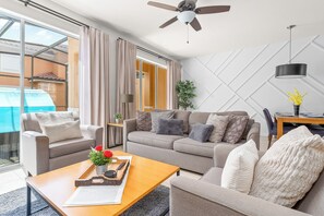 Una sala de estar moderna con un sofá, sillones, una mesa de centro y un ventilador de techo.