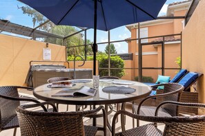 Une terrasse extérieure avec une table en verre, des chaises en osier, un barbecue et un parasol bleu.
