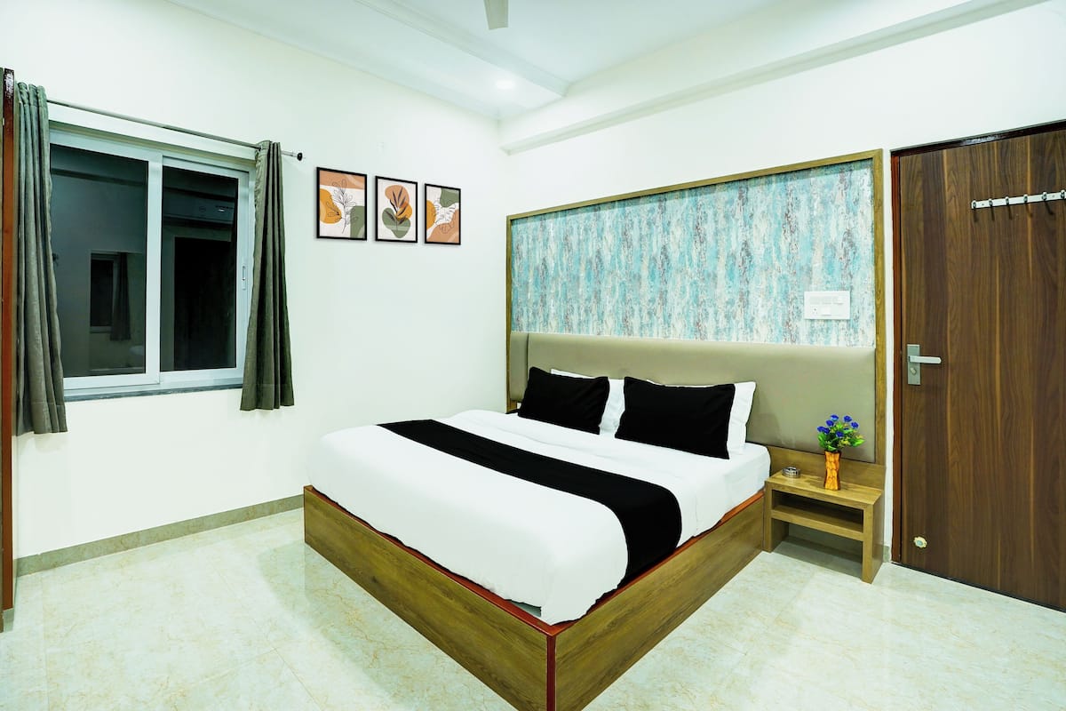A bedroom with a bed, a nightstand, a window with curtains, a door, and wall art.