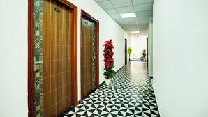 A hallway with patterned flooring, wooden doors, and a potted plant. - Hotel Jai Palace & Guest House (Jaipur)